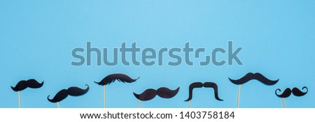 Various black photo booth props moustaches of different shape on blue background. Greeting card for father's day or men's health awareness month campaign concept. Flat lay, banner