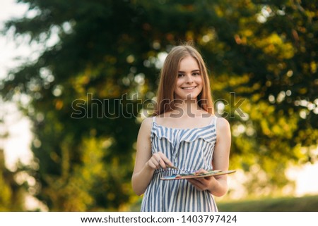 Portrait of Beautiful girl artist is standing in the park and holding palette with paints