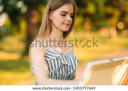 Portrait of Blond hair girl in dress drawing a picture in the park