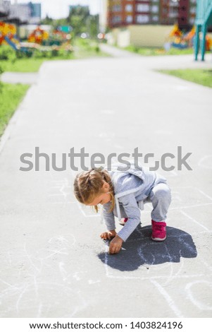little girl draws on asphalt and plays hopscotch
