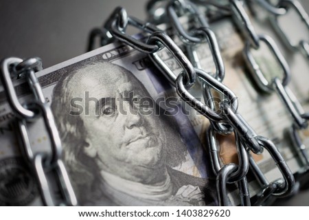 chained money, a bundle of dollars tied up with a chain, the concept of credit slavery, debt, frozen assets. dark background, closeup Royalty-Free Stock Photo #1403829620
