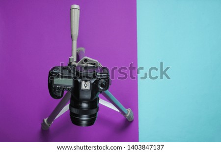Modern digital camera with tripod on blue purple background. Top view