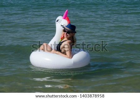 Smiling woman floating on inflatable unicorn pool float on sea
