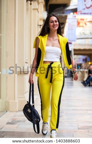 Portrait of a young beautiful girl in a white top and yellow sports pants posing in a mall