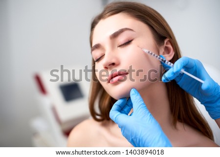Beautician doctor with botulinum toxin syringe making injection to to remove crow's feet. Cheek volume enhance mesotherapy. Anti-aging treatment and face lift in cosmetology clinic. Royalty-Free Stock Photo #1403894018