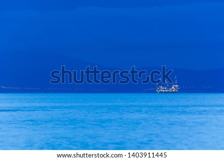 Big offshore oil rig drilling platform complex with anchored ship at dusk, with continent in background, Aegean Sea, Greece