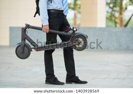 Close-up of businessman holding electric scooter in his hand while standing outdoors in the city Royalty-Free Stock Photo #1403928569