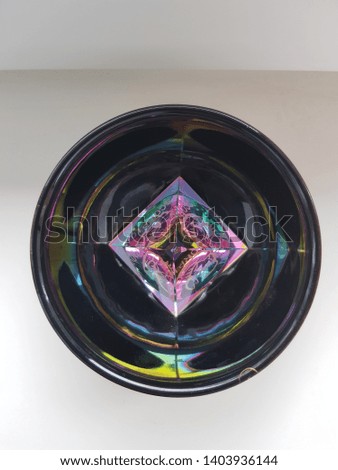 The art of Abstraction in the Photo: a transparent glass pyramid with a multi-colored pattern inside a dark glass bowl and reflected in it with colored circles (top view)
