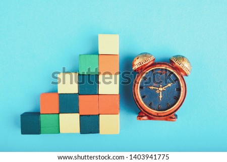 Time management concept, miniature alarm clock and wooden cube on blue background.