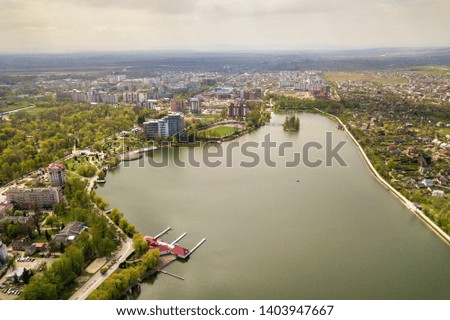Aerial view of city lake among green trees and town buildings in recreation park zone. Drone photography.