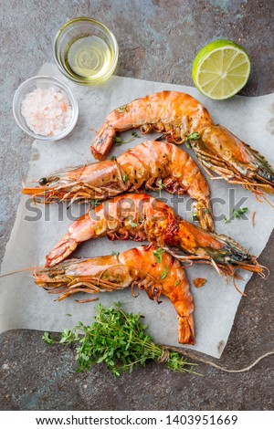 Grilled giant tiger prawns on paper with lemon and spices on vintage dark background, top view, copy space. Seafood dinner.
