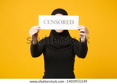 Young arabian muslim woman in hijab black clothes hold in hands sign with censored title isolated on yellow wall background, studio portrait. People religious lifestyle concept. Mock up copy space