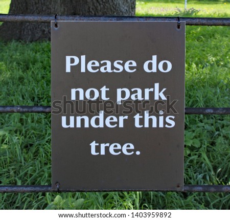Sign fixed to a gate in a wood, warning visitors not to park under this tree.