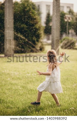 a little girl runs on a green lawn, smiles genuinely and plays in the summer, dressed in a white dress, but around the water spills out of the lazano
