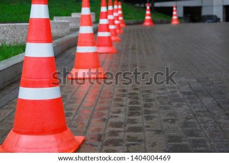 Row of orange traffic cones with white stripes on brick road 