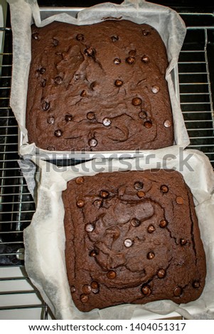 Two chocolate brownies on a metal baking tray in a baking form with baking paper in between pastry and baking form close up top view picture