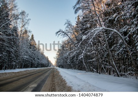 The road in the winter forest. Snow picture. Branches of trees in the snow hang over the road.