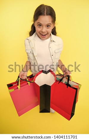 Check out her profitable purchases. Girl carries shopping bags yellow background. Girl fond of shopping. Child cute shopaholic with bunch shopping bags black friday total sale. Exciting shopping.
