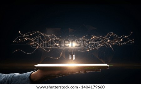 Hand holding tablet with creative glowing lamp on dark background. Idea and science concept.