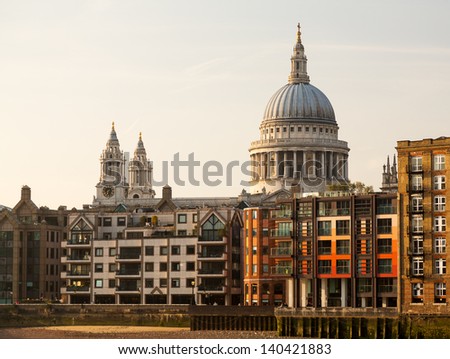 Modern apartments and homes by river Thames with St Pauls Cathedral in London England at dusk as the sun is setting low in sky.
