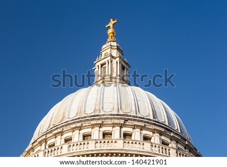 Golden cross on dome of St Pauls Cathedral in London England at dusk as the sun is setting low in sky.