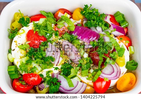 Large portion of seasoned Halloumi or Feta cheese with many fresh herbs, tomatoes and red onions in a casserole dish for grilling in the oven or on the grill for a barbecue