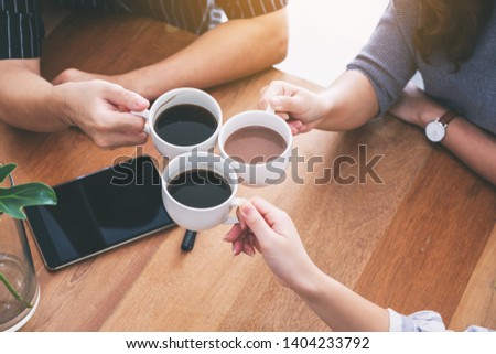 Close up image of three people enjoyed drinking and clinking coffee cups on wooden table in cafe