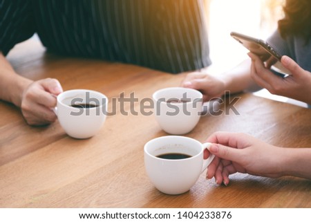 Closeup image of three people holding coffee cups to drink on wooden table