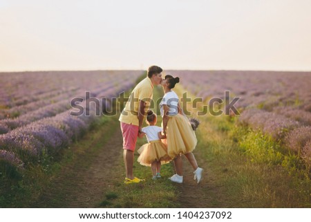 Young family in yellow clothes walk on purple lavender flower meadow field background, have fun, play with little cute child baby girl. Mother father, small kid daughter. Outdoors summer day concept