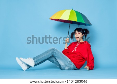 woman sitting on the floor in a red sweater with umbrella against a blue background                              