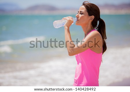 Cute young woman taking a break from running and drinking water from a bottle