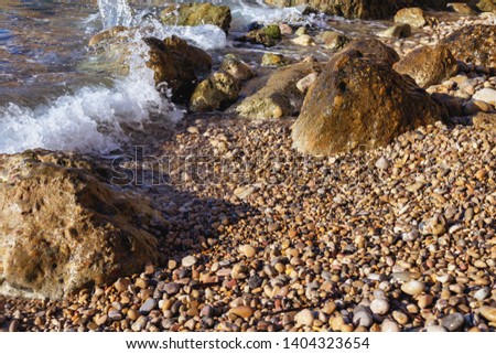 a fragment of a sunny rocky beach with small and large stones and a moving sea wave