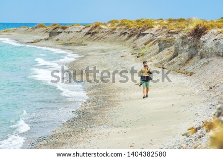 A man with photographic equipment walks along the shore of Issyk Kul lake in Kyrgyzstan. Photographer-traveler walks along the lake. The guy with the camera on his shoulder goes along the shore.