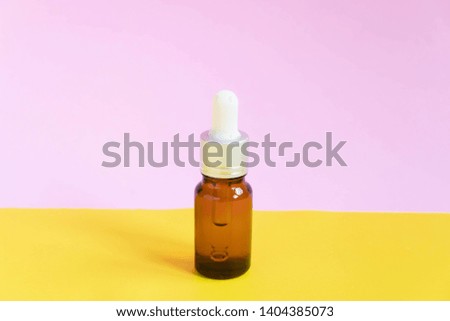 Brown glass bottle w/ dropper on yellow pink background. Packaging of serum or essential oil. Minimal style.