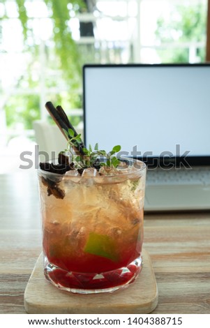 Cocktail with ice in a glass in front of business laptop background on the table in a cafe and  face to summer garden view.