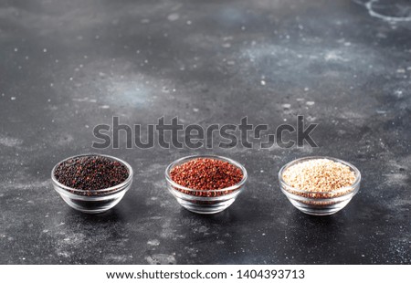 Black, white and red quinoa in bowls, raw quinoa groats assorted, gray kitchen table, selective focus