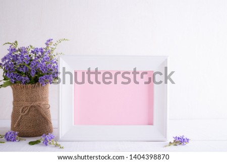 Happy mothers day concept. White picture frame with lovely purple flower in vase on white wooden table.