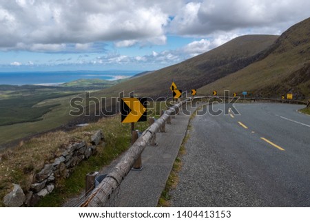 Looking along the empty winding road of the Conor Pass on the Dingle Peninsula, Ireland, bright blue sky with fluffy clouds. Royalty-Free Stock Photo #1404413153