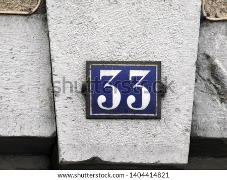 House number thirty three (33) sign white on blue plate against stone background. Grunge, texture, wallpaper