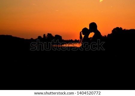 Silhouettes of a kissing couple in nature with clear orange sky before sunset