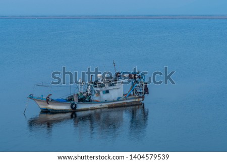 Fishing boat at anchor alone in ocean waters under blue sky.