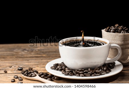 Fresh coffee in a white coffee cup with roasted coffee beans on the plate And having a coffee bean in a sack placed on an old wooden table on a black background - a picture