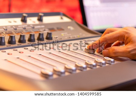 sound engineer fingers adjusting volume level fader on digital mixing console. music production, recording, broadcasting, music concept