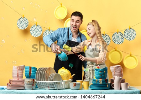 excited cheerful couple washing plates, bowels, cups by hand at home,bubbles flying in the room Royalty-Free Stock Photo #1404667244