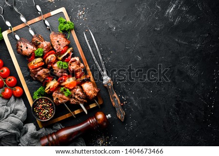 Shish kebab BBQ meat with onions and tomatoes. On a black background. Top view. Free space for your text. Rustic style. Royalty-Free Stock Photo #1404673466