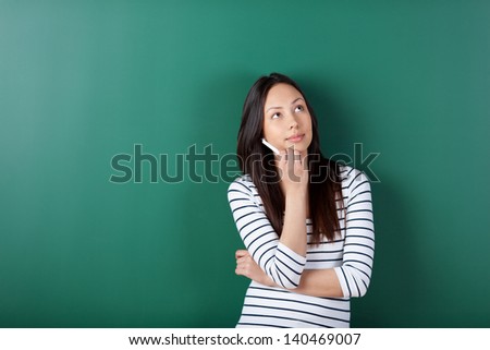 thoughtful female student leaning against blackboard in school