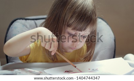 Cute little girl with a brush and paints. Caucasian. looks with his big blue eyes and smiles. Long blonde hair in a two year old child.