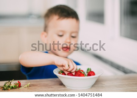 A child, a boy in the kitchen eating strawberries very appetizing and tasty, stocked with vitamins
