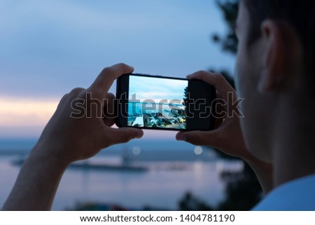 Men's hands holding smartphone and taking photo of beautiful sunset on the beach