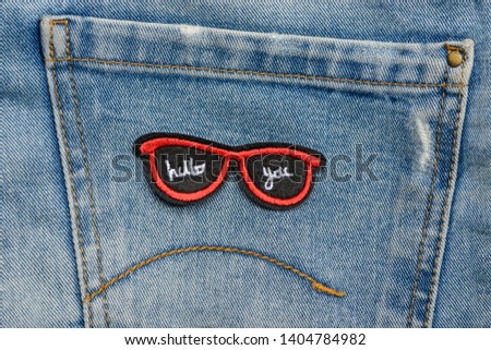 Close up on red sunglasses embroidered patch on a pocket of blue jeans. Custom design for denim wear.
